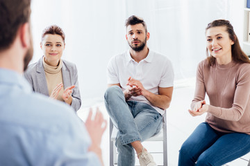 selective focus of people applauding while looking at man during group therapy session
