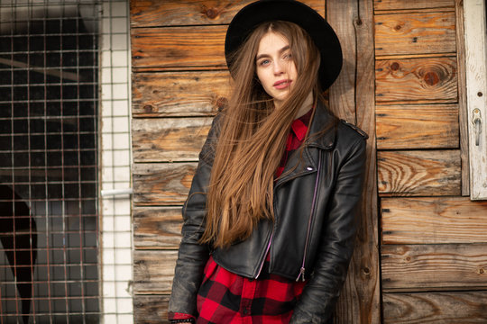 Beautiful girl with long hair and black hat, stands on the background of vintage old wooden house.