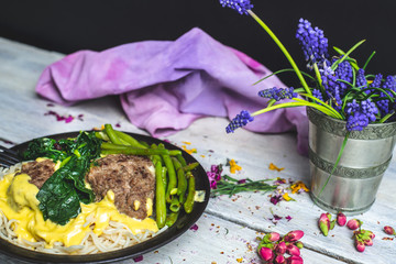 in a bright, rustic kitchen, on a wooden table lies a plate of spaghetti with cheese sauce, garlic, meatballs, spinach and green bean stew