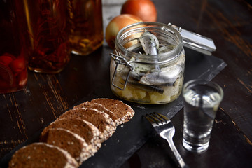 marinated herring with onions in a glass jar, on a dark background