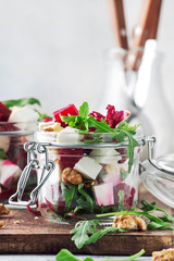 Beet salad with arugula, goat cheese and nuts, trendy salad jar, gray kitchen table background, selective focus