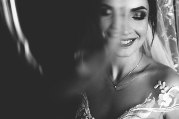 Beautiful closeup portrait of bride. Girl stand in luxury wedding dress near window. Black and white