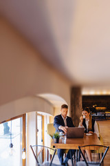 Obraz premium A stylish couple drinks morning coffee at the cafe and works with a laptop, young businessmen and freelancers