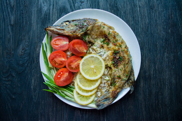 Baked pike in the oven, decorated with vegetables and herbs. Serving on a plate. Proper nutrition. Dark wood background.