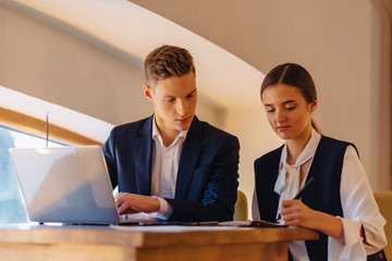 young businessmen boy and girl work with a laptop, a tablet and notes in the cafe