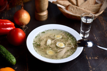 chicken soup with quail eggs in a white plate on a wooden background