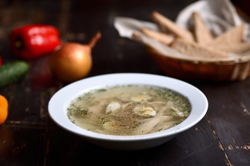 chicken soup with quail eggs in a white plate on a wooden background