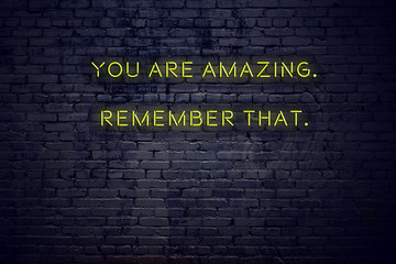 Positive inspiring quote on neon sign against brick wall you are amazing remember that
