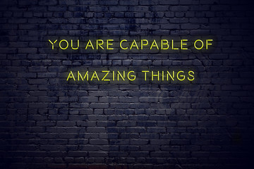 Positive inspiring quote on neon sign against brick wall you are capable of amazing things