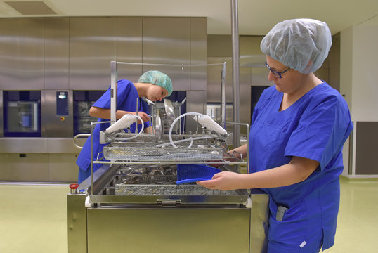 Two women work in a hospital as medical hygiene  technicians. They are dressed in special medical  hygiene clothing. They are seen carrying out hygiene  disinfecting and sterilization tasks.
