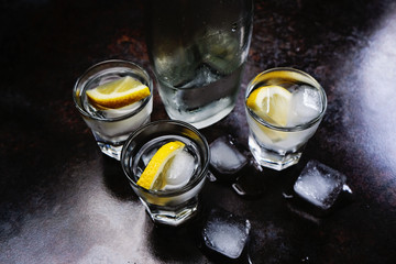 Vodka. Shots, glasses with vodka and lemon with ice .Dark stone background.