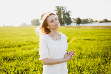 Girl enjoying nature on the field in the rays of sunlight. Beautiful model girl in a white dress on the field in the light of the sun. Sun Glow. Free happy woman outdoors
