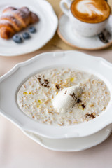 Bowl of breakfast oatmeal with soft Italian cheese and cinnamon. Croissants, coffee and other dishes on the table in the restaurant