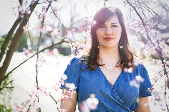 Portrait of brunette woman standing near cherry blossom tree