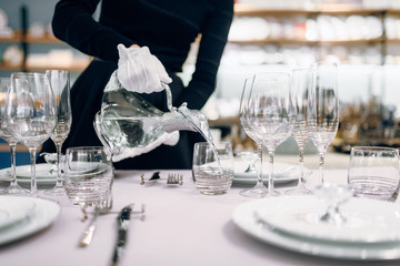 Waitress pours drinks into glasses, table setting - Powered by Adobe