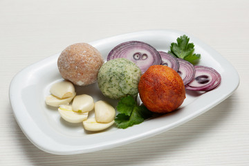 Three balls of snack from lard, with the addition of garlic and red pepper, next to pieces of garlic and onion, sliced into rings