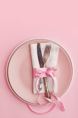 Elegant stylish table setting. Knife and fork on a napkin on a plate on a pink background.