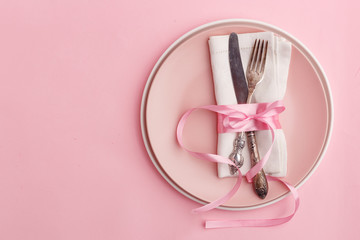 Elegant stylish table setting. Knife and fork on a napkin on a plate on a pink background.