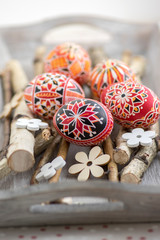 Fototapeta na wymiar Homemade handmade painted Easter eggs on birch branches on grey wooden tray, traditional hnadcraft eggs, white flowers