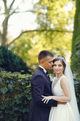 Elegant bride in a white dress and veil. Handsome groom in a blue suit. Couple in a summer park