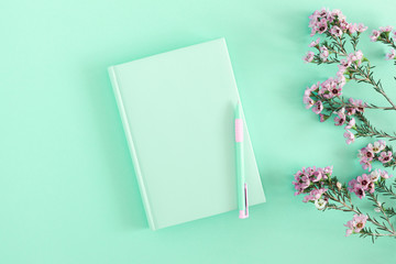 Light green notebook, pen and pink flowers on light green desk. Business minimal concept for women....