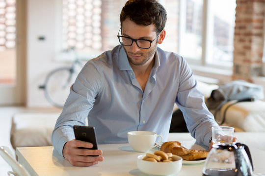 Young man using smartphone white sitting at dining table in home