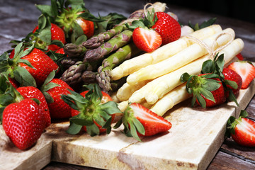 White and green asparagus with strawberries on wood