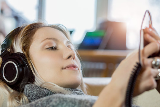 Close up of young woman with bleached hair listening to music while lying indoors