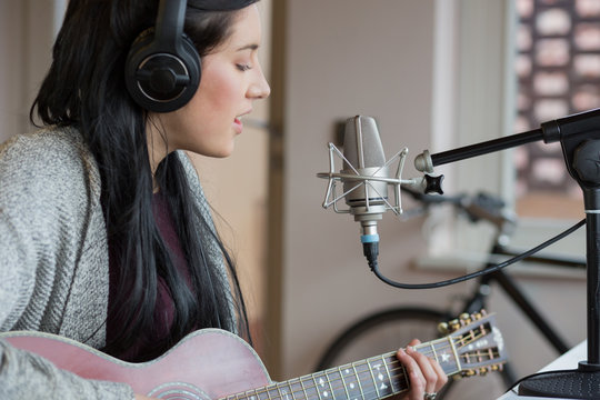 Woman with black hair singing while playing guitar in studio