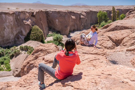 Two women taking photos of an amazing Atacama Desert valley at Toconao town, an awe canyon with beautiful scenery illuminated by sunlight. An awe arid landscape with a river from Andes mountains
