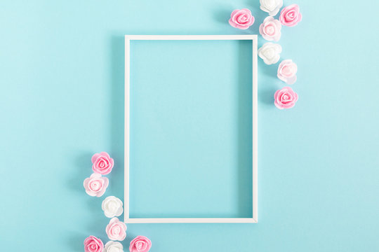 Flowers composition creative. Blank photo frame, pink and white artificial flowers on pastel blue background. Flat lay, top view, copy space