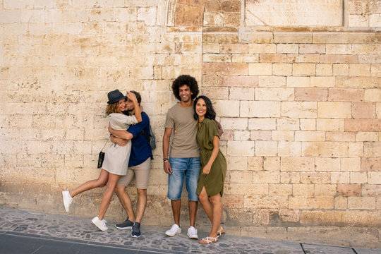 Smiling young couples embracing while standing against brick wall
