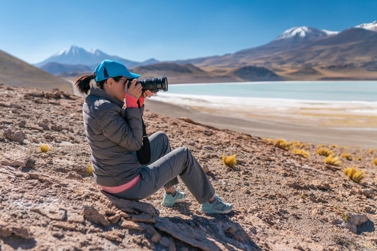 Landscape woman photographer taking photos in an amazing wilderness environment at Atacama Desert Andes mountains lagoons. A woman cut out silhouette over the awe Tuyajto Lagoon scenery at Altiplano
