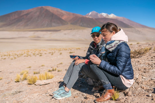 Two women outdoor photographers taking photos at Andes Altiplano, awe mountain scenery at Atacama Desert. An arid landscape full of salt flats and lakes with beautiful volcanic scenery on a sunny day
