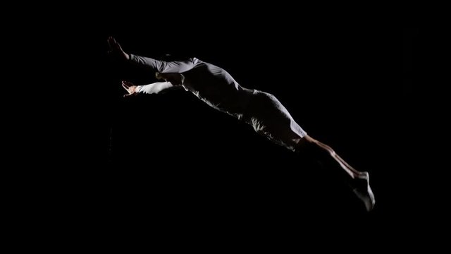 Athletic man in white clothes performs tricks jumping on a trampoline on a black monophonic background