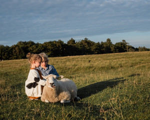 Zwei Kinder streicheln ein zutrauliches Schaf auf der Wiese eines Bauernhofes
