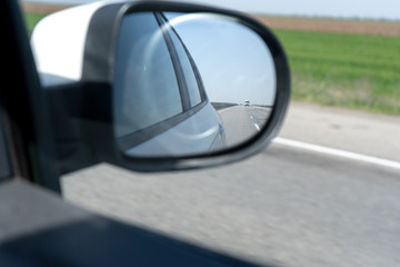 The track in the front view mirror of a white car. Journey to the South of Ukraine on a hot cloudless spring day