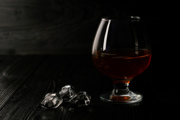 Cognac in a glass on a wooden background with ice