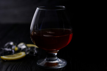 Cognac in a glass on a wooden background with ice and lemon