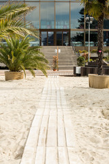 Fototapeta na wymiar Wooden pathway through beach to modern glass building