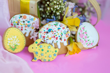 Fototapeta na wymiar Flat lay Easter treats gingerbread cookies in the form of Easter cake, Easter eggs and rabbits decorated with glaze with spring flowers on a pink background with place for text