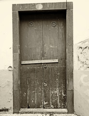 sepia vintage style image of a closed wooden door locked and barred shut with nails with peeling paint and stone surround