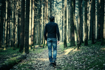Fototapeta premium Lonely man walking down the mystery forest path between trees.