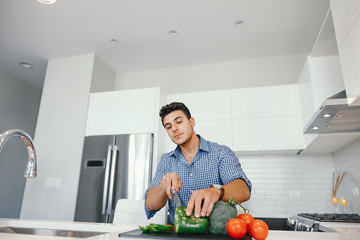 Man in a kitchen. A handsome man cut the tomatoes with a knife. Male at home with vagatables.