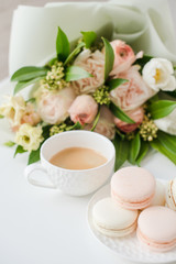 Elegant sweet dessert macarons, cup of coffee and pastel colored beige flowers bouquet