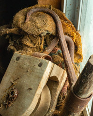 close up of antique wooden pulley, rusty hay hook, and dusty burlap feed sack in old barn window