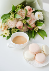 Elegant sweet dessert macarons, cup of coffee and pastel colored beige flowers bouquet