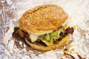 Bad-looking fast food hamburger on a silver wrapping paper. Ugly food. Unhealthy USA/ American habits. Poverty lifestyle. 