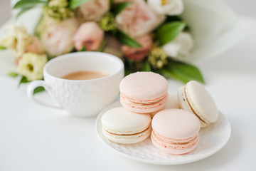 Elegant sweet dessert macarons, cup of coffee and pastel colored beige flowers bouquet
