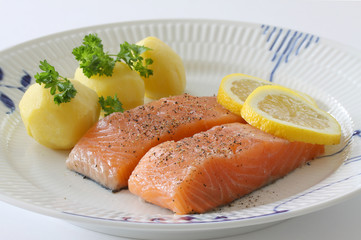 Salmon fillet with potatoes, lemon slices and parsley served on a plate. Close up stock photo.